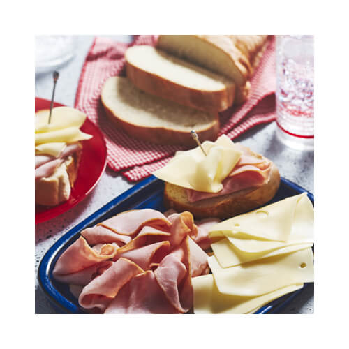 Speckled marble countertop with blue plate of French loaf slices, Swiss cheese slices and deli meat.
