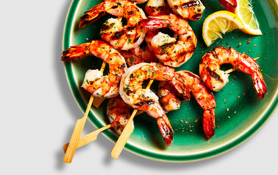 round green plate with three cooked shrimp skewers laid on top, and cut limes for garnish