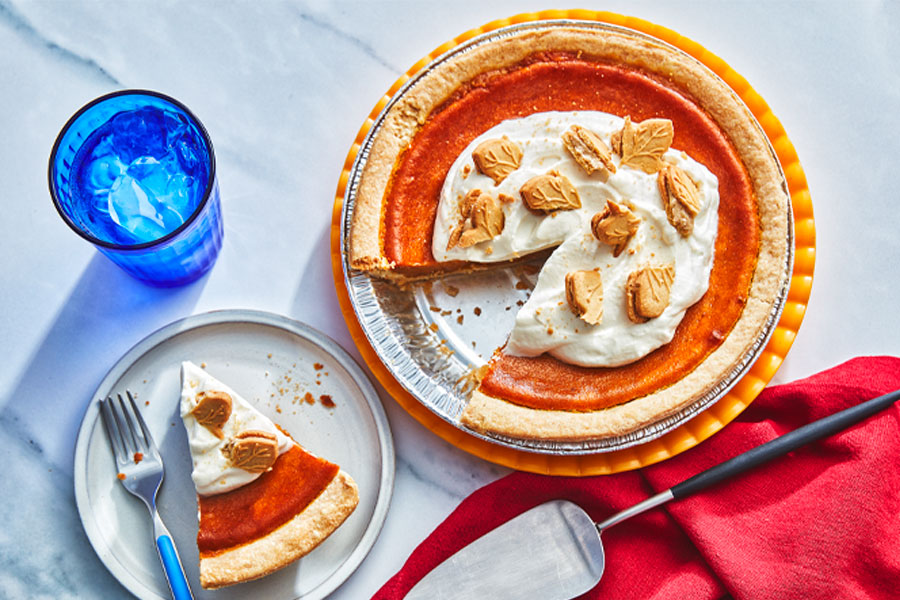 Pumpkin pie, topped with whipped cream and cookies, with a side plate of a slice of pumpkin pie and a pie server