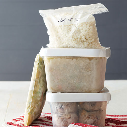 Filled containers and freezer bags of frozen foods with date labels on a grey counter.