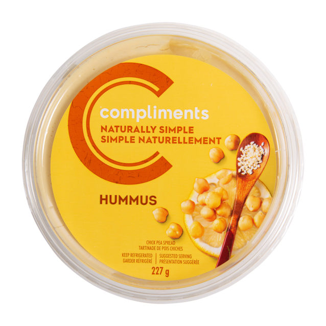 A plastic container of Compliments Naturally Simple Traditional Hummus with a yellow and orange sticker on the front.