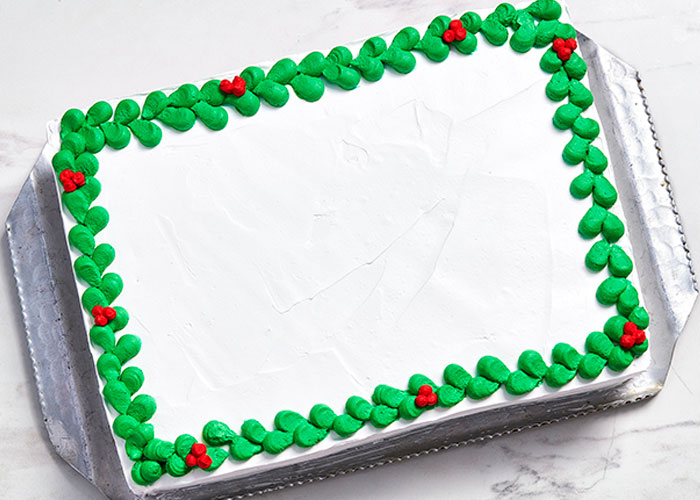 white rectangular cake with holly icing around the edge, and blank centre ready for customized message.