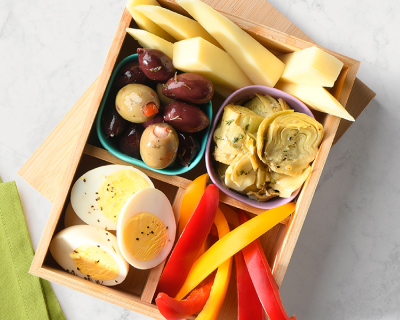 Wooden bento box featuring vegetarian options including olives, cheese, marinated artichokes, bell pepper slices and hard-boiled eggs.