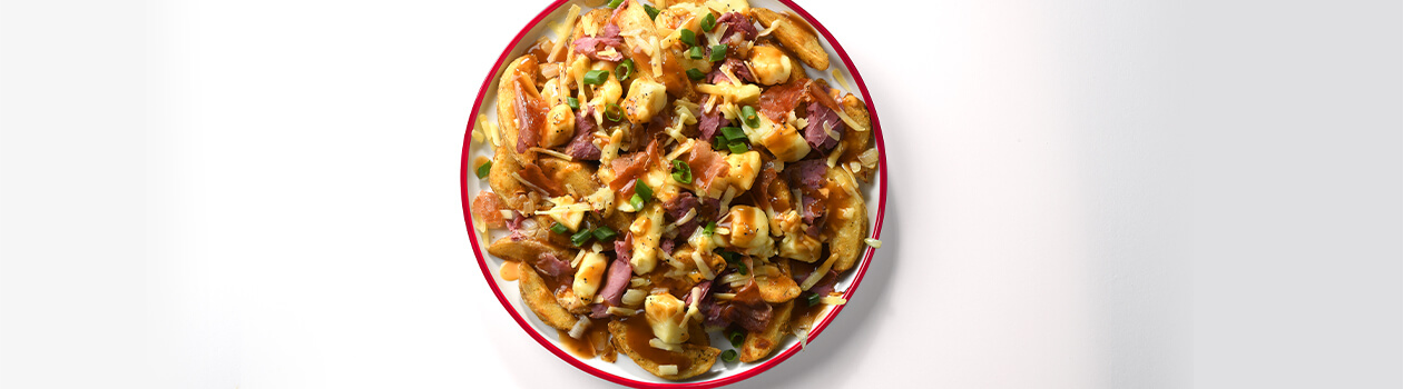 White plate with a red rim full of poutine topped with melted cheese curds, sausage pieces and gravy.