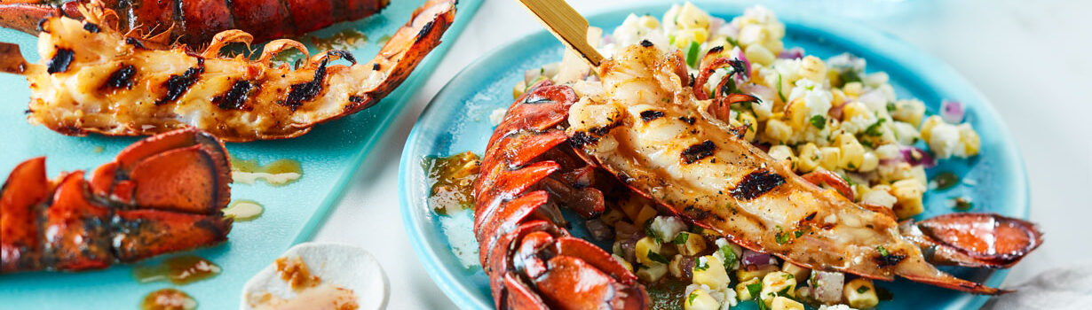 Jerk spiced lobster tail on an aquamarine blue plate next to a charred corn salad.