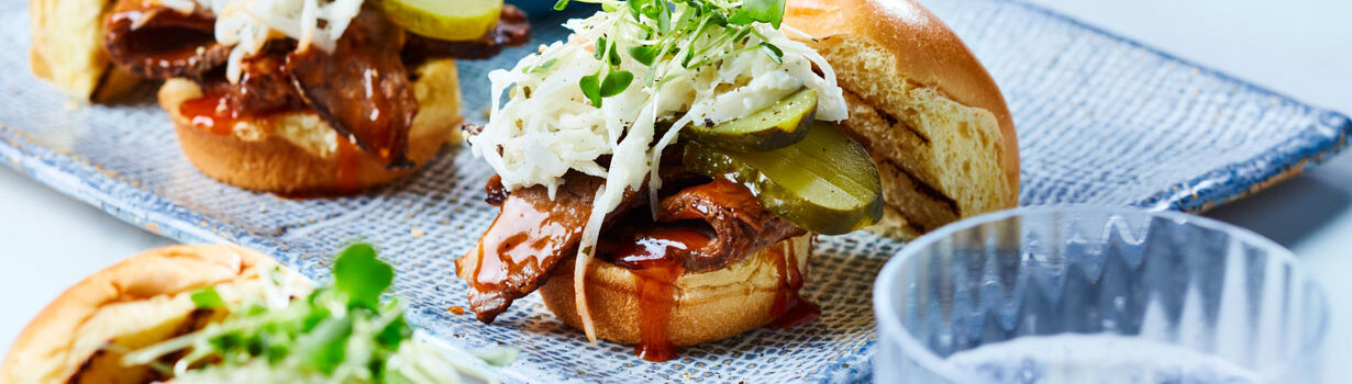 BBQ brisket sliders topped with creamy coleslaw and microgreens on a blue plate.
