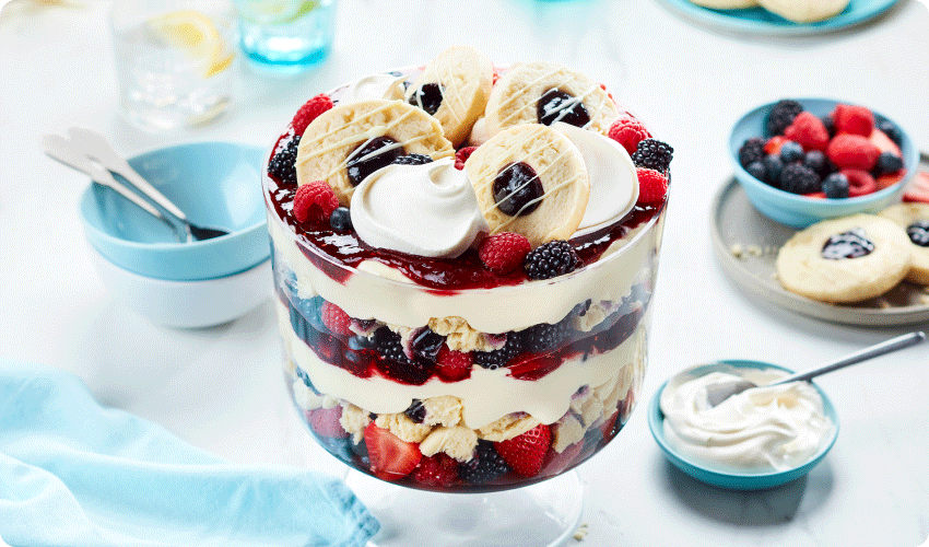 large trifle dish with layers of vanilla pudding, crumble and whole blueberry sugar cookies, fresh berries and whipped cream