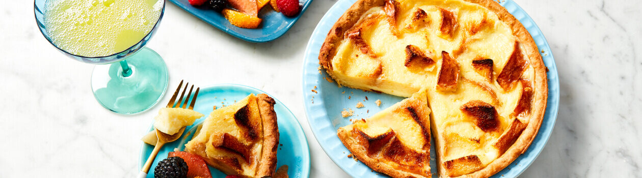 Brioche pudding pie in a pale blue pie plate next to a serving on a blue plate with fresh fruit.