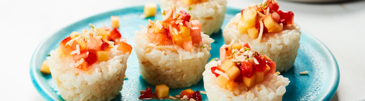 Fruit topped rice rolls like sushi, on a light blue plate.