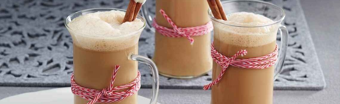 A grey table with three clear mugs of Gingerbread Almond Latte with cinnamon stir sticks and red and white twine wrapped around the middle.