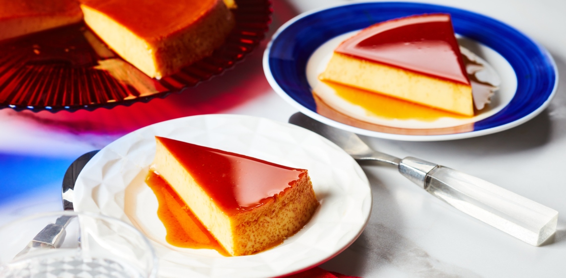 large red serving platter with caramel-topped round Mexican-style flan with two slices cut, one served out on blue-rimmed white side plate at right