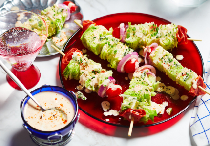 Red serving platter with five wedge salad skewers, and a side dish of dressing with a spoon dipped in