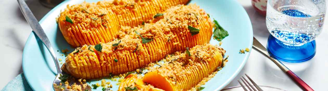 Aqua blue serving platter with three halves of roasted butternut squash, cut in hasselback-style and topped with sage and breadcrumbs