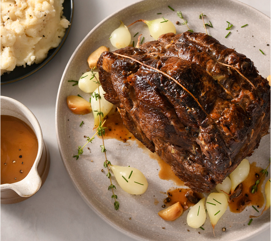 Blade pot roast on plate with pearl onions and side of mashed potatoes