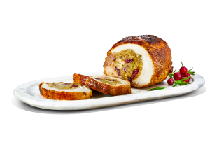 A turkey roast stuffed with pork, cranberry, and apple stuffing on a long oval plate with fresh cranberry and herb sprigs