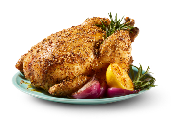 A whole, seasoned chicken roast with herbs, half a lemon, and pieces of onion on a plate